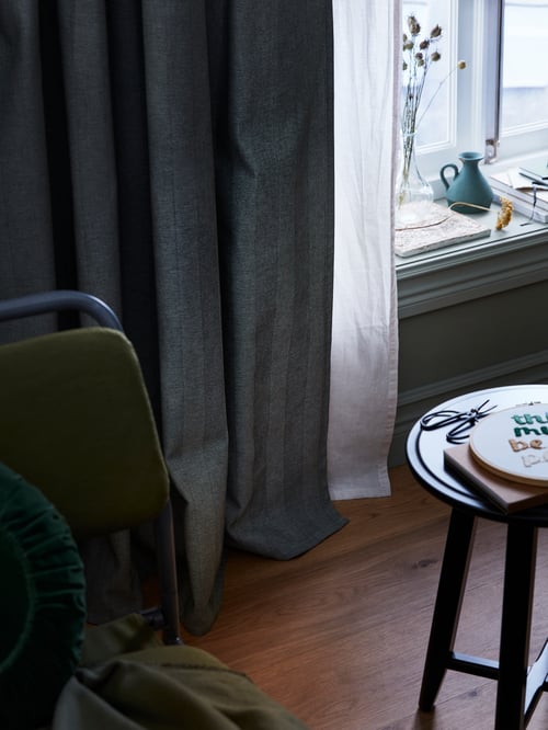 Partial shot of a pair of room darkening curtains, a standard pair of curtains, and a round table with items on the tabletop.