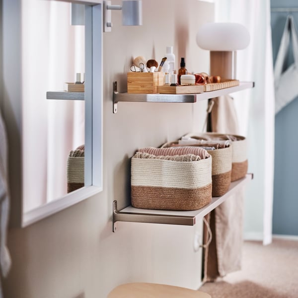 Two shelves on a wall with a white NISSEDAL mirror and a KYRRE stool by them. The lower shelf holds three LJUNGAN baskets.