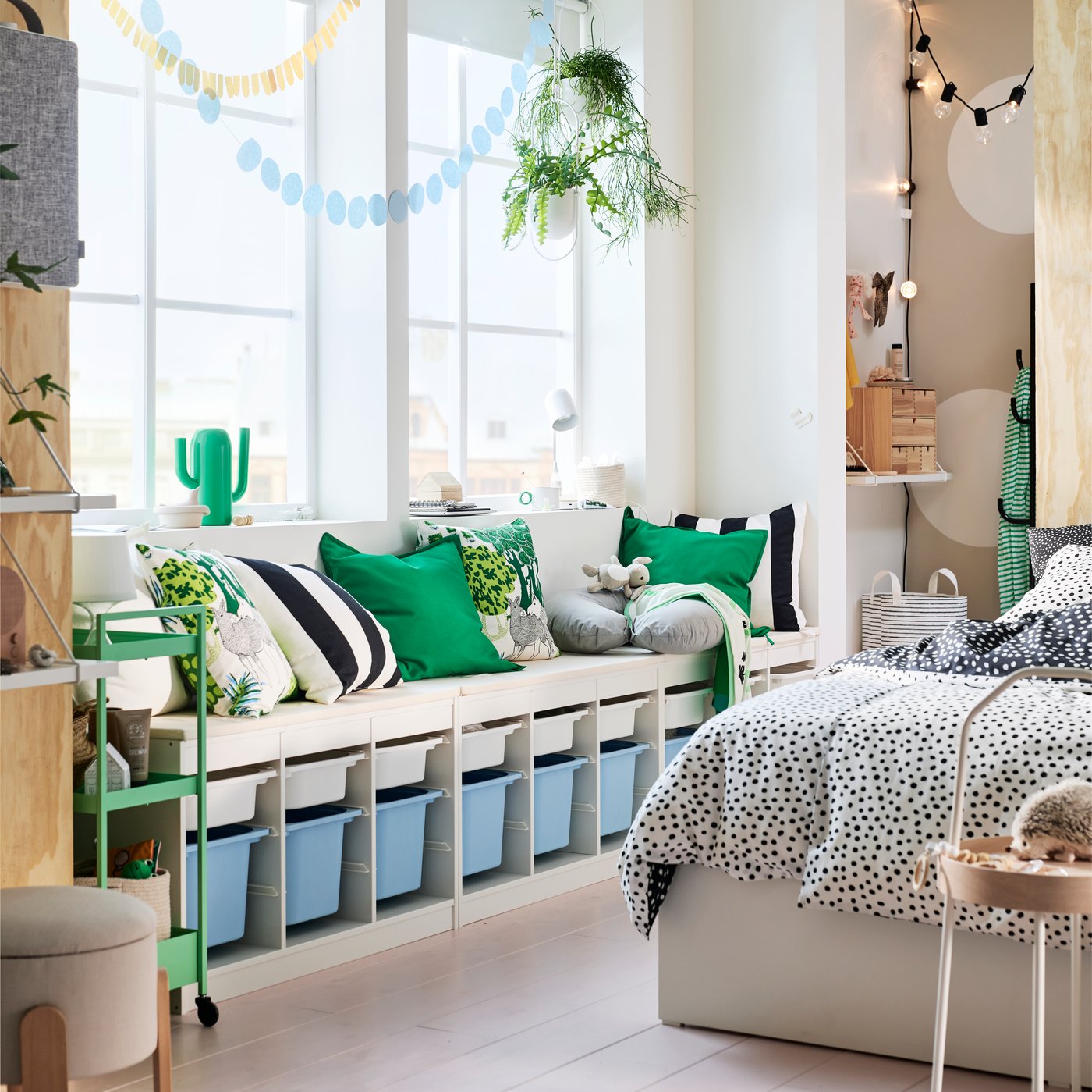 Trois structures TROFAST blanches côte à côte contenant des bacs TROFAST bleu clair et blancs, près d’un lit VIHALS, sur un sol rose.