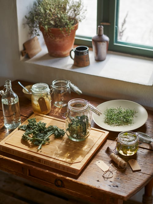 In a kitchen, there is an APTITLIG butcher's block, with herbs and a jar with lid on top, next to other jars and herbs.