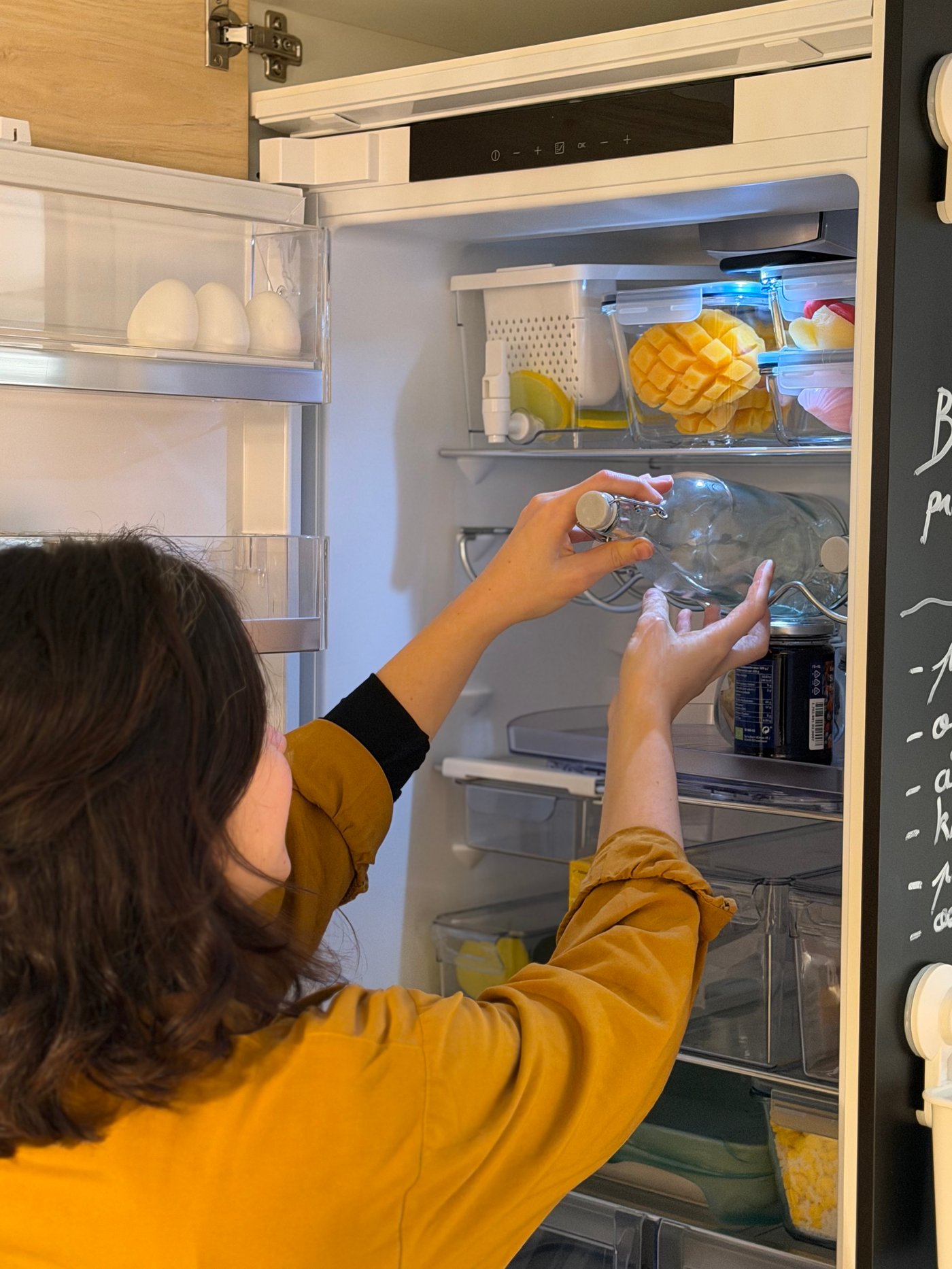 Aline de @studiogubri prenant une bouteille d'eau en verre dans son réfrigérateur