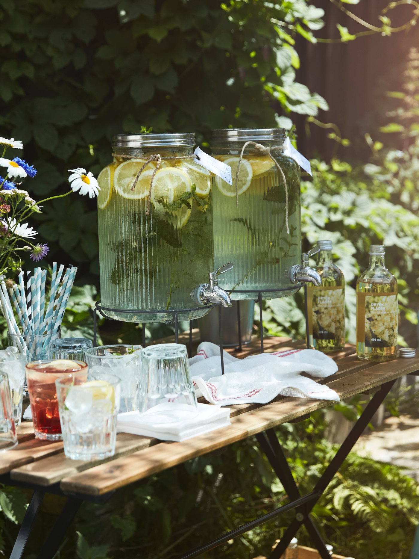 A small garden table set with glasses, straws, and lemonade in a VARDAGEN jar with tap, ready for guests at a party.