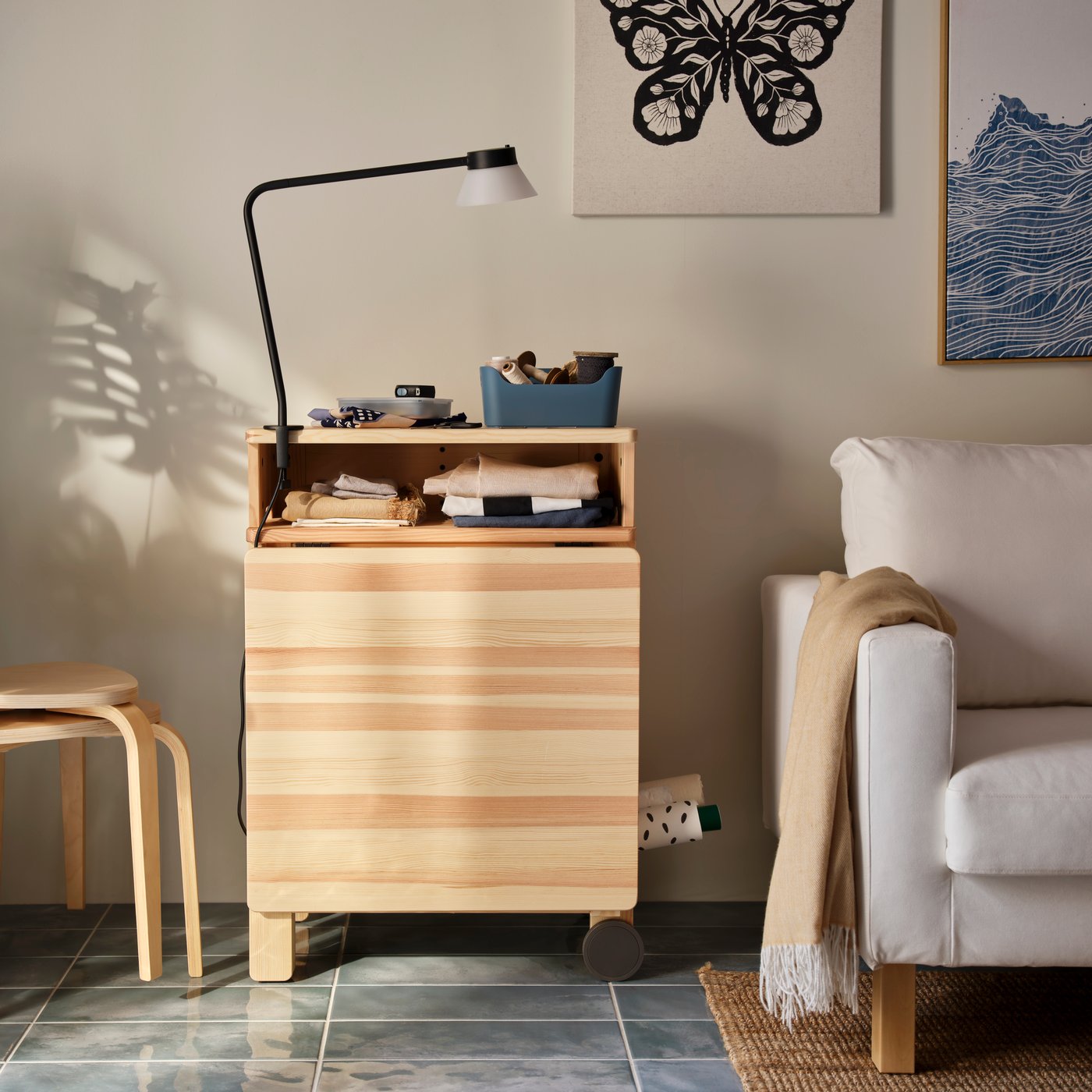 A sunlit living room with a pine RESARÖ mobile drop-leaf table in folded mode, by a wall and next to a SALTSJÖBADEN armchair.