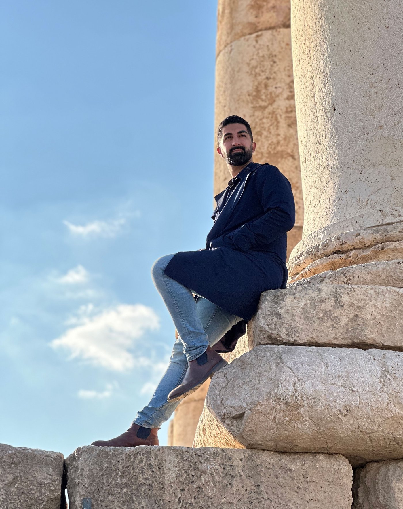 Arash outside on a sunny day, leaning against a large pillar.