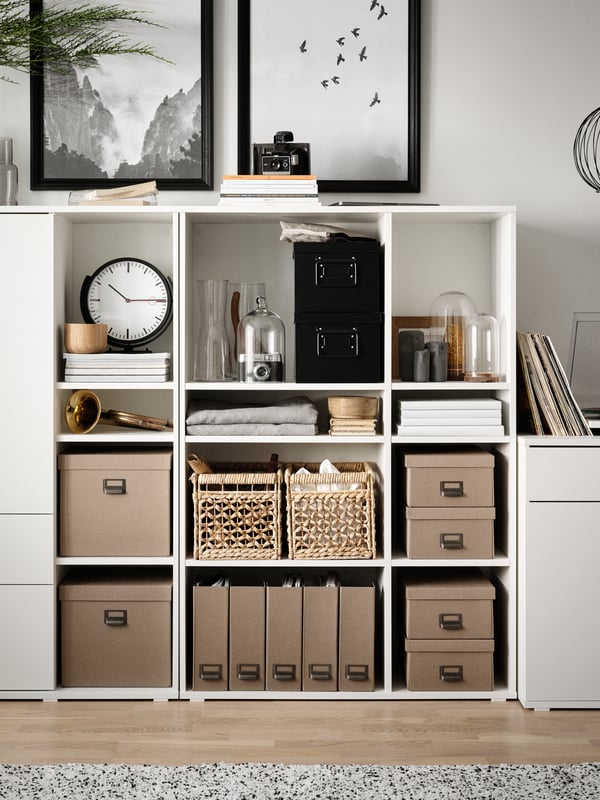 Two white VIHALS open shelving units side by side filled with storage boxes, baskets and other objects including a clock.