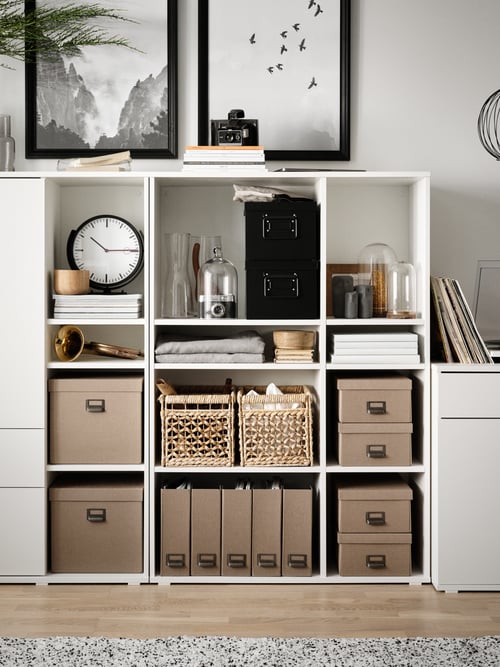 Two white VIHALS open shelving units side by side filled with storage boxes, baskets and other objects including a clock.