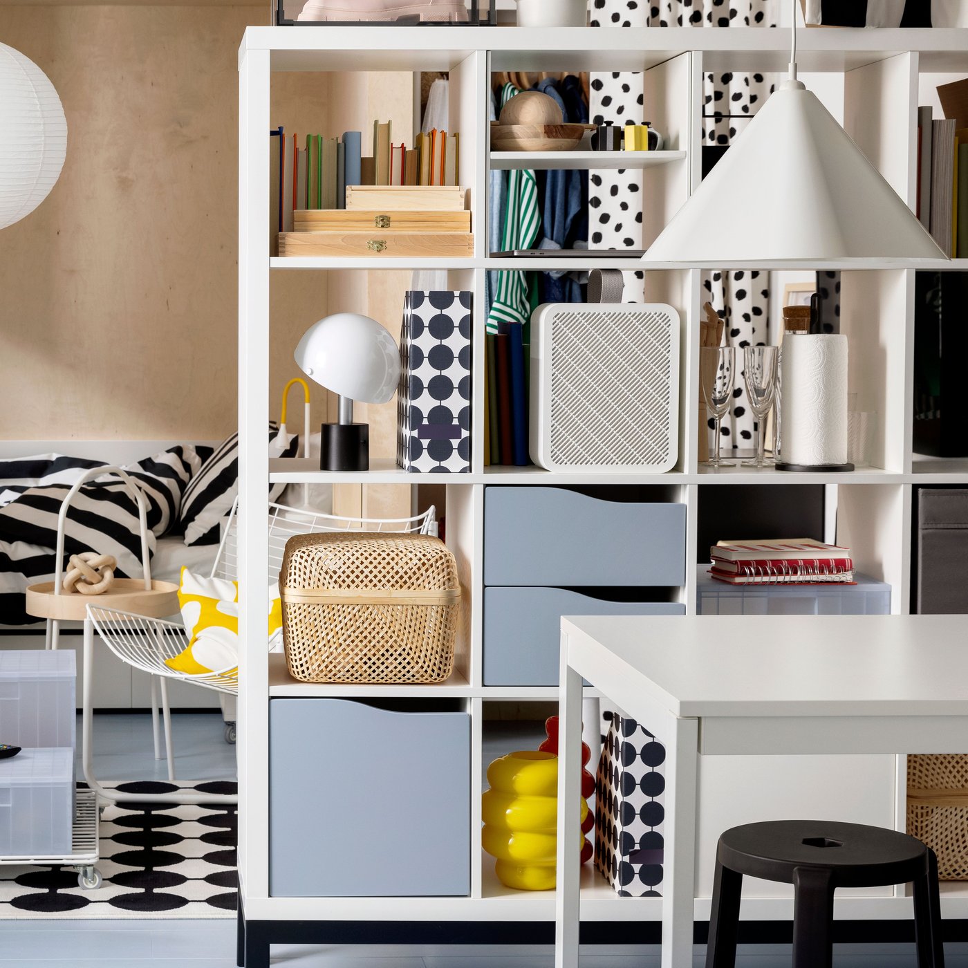 Salon avec une étagère KALLAX servant de séparateur de pièce, remplie d'objets de rangement, de livres et d'objets décoratifs.