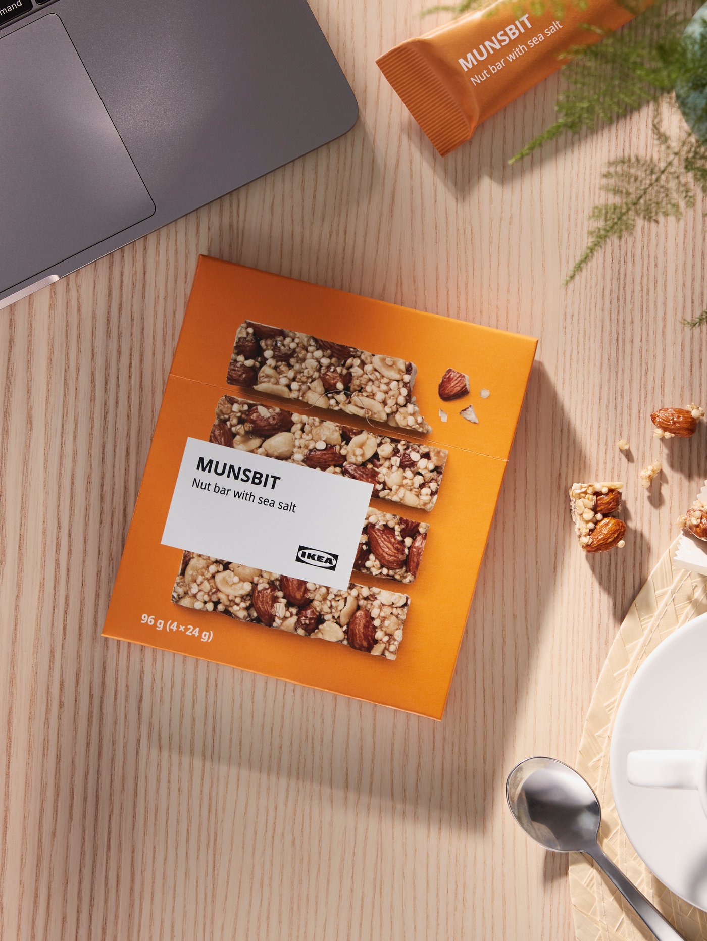 An orange MUNSBIT package containing nut bars on a wooden surface next to a cup of coffee and a laptop.