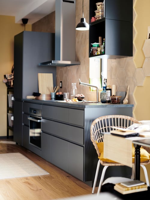 Kitchen with grey base cabinets, chair, table, oven, extractor hood, open cabinet, mixer tap, pendant lamp, food containers.