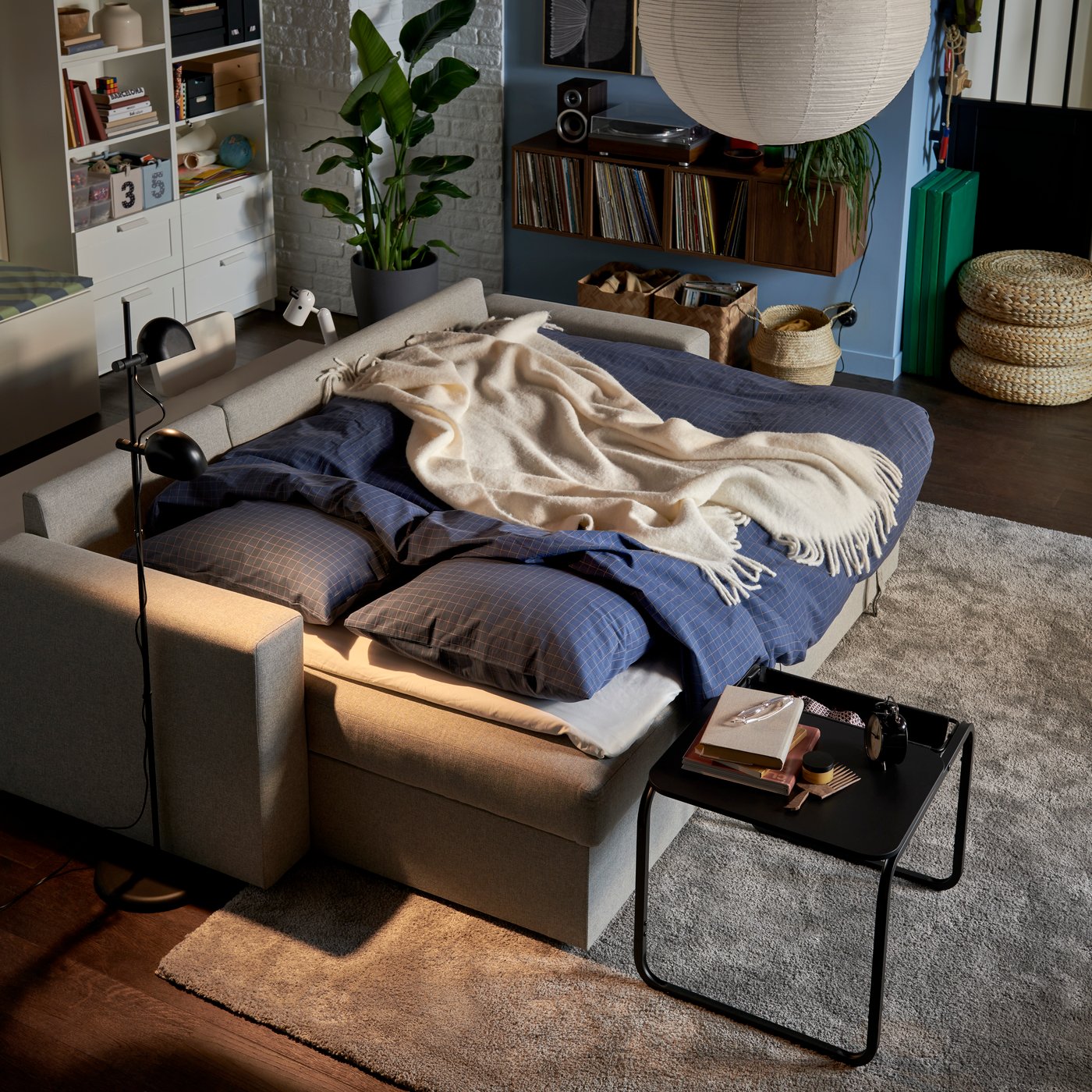 A dimly lit living room with a BÅRSLÖV sofa-bed made for the night with DOFTAKLEJA duvet cover and pillowcases.