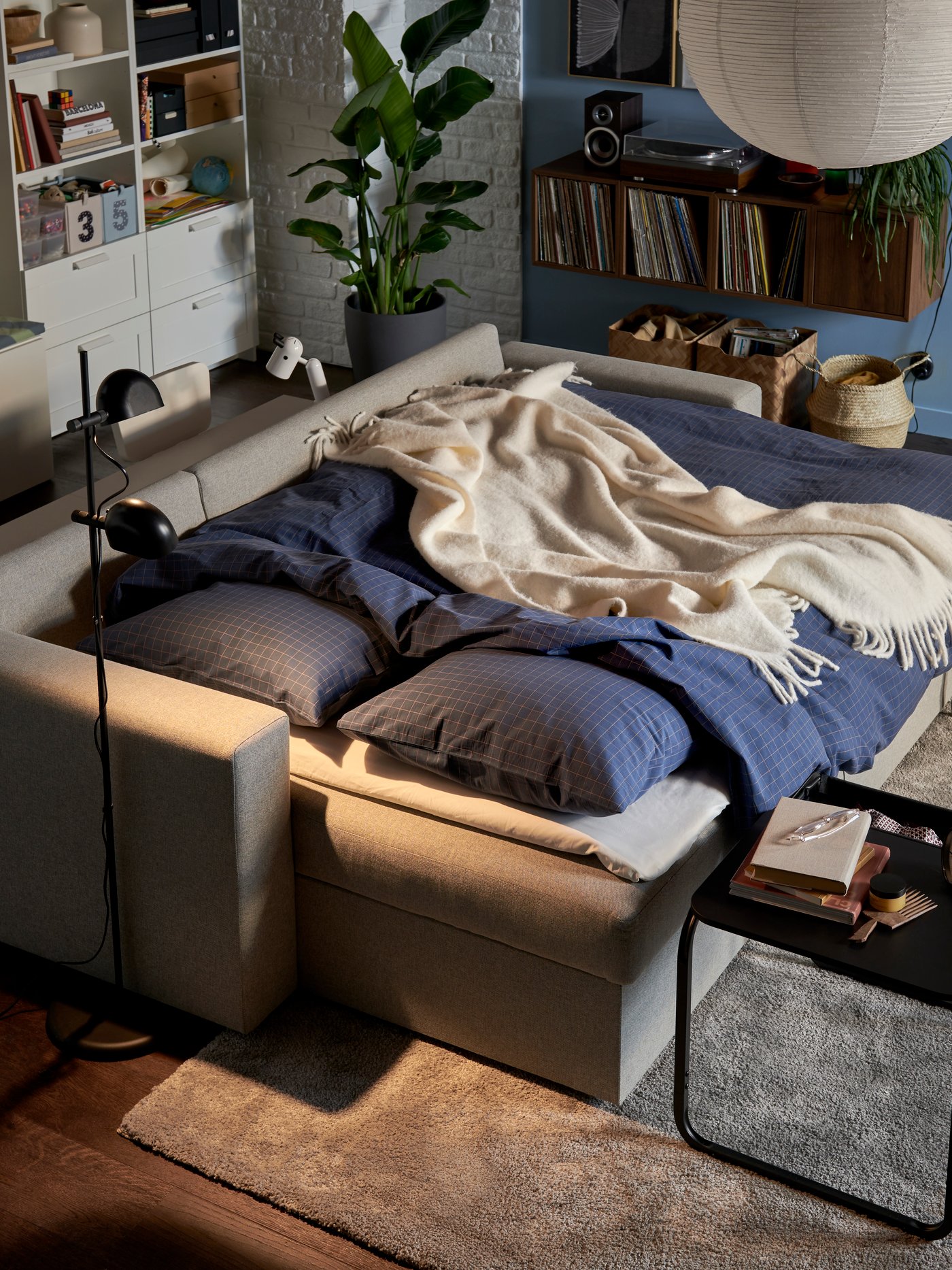 A dimly lit living room with a BÅRSLÖV sofa-bed made for the night with DOFTAKLEJA duvet cover and pillowcases.