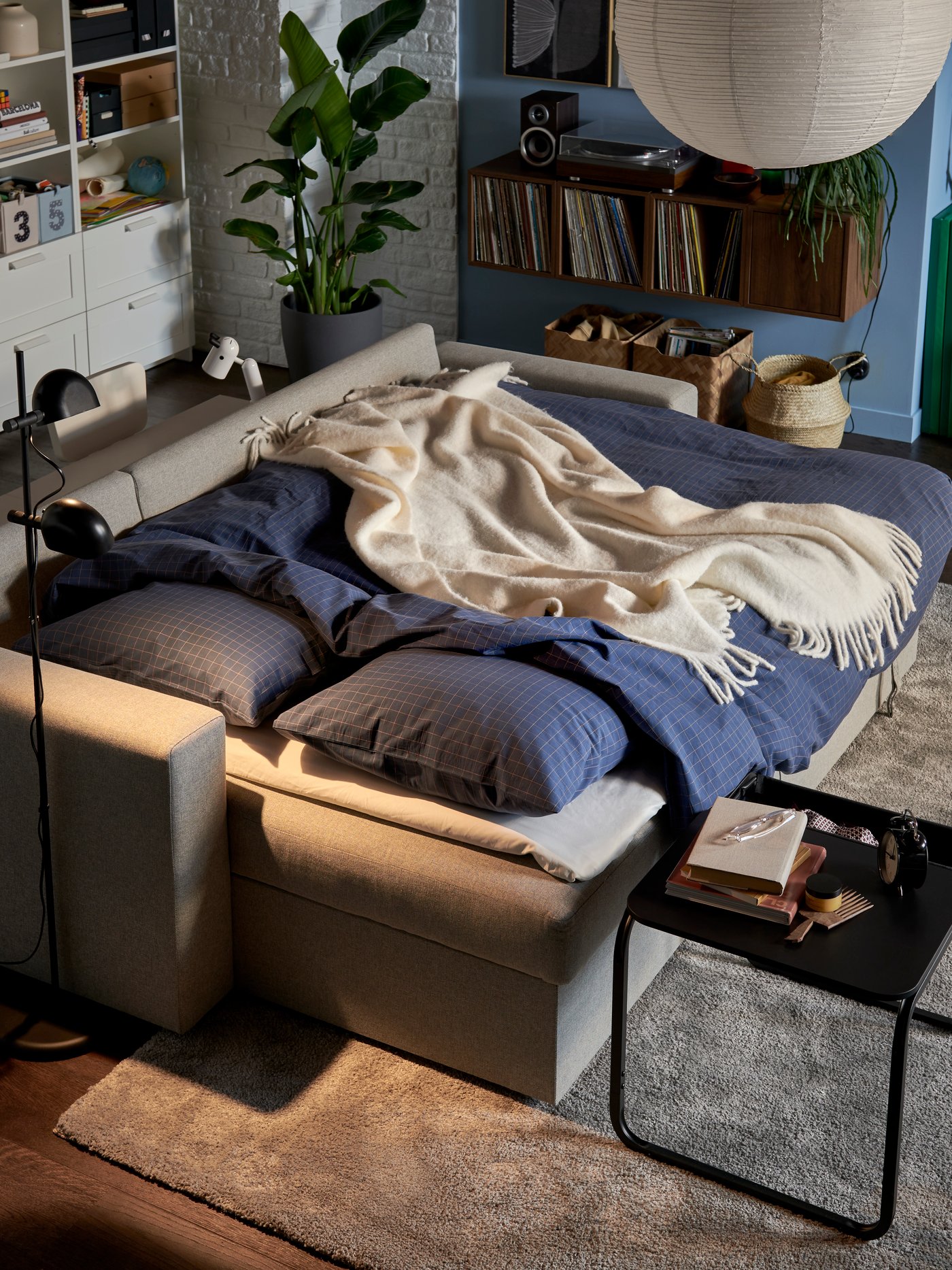 Ein hellgraues BÅRSLÖV 3-Sitzer-Schlafsofa bedeckt mit Bettdecke und zwei Pölstern gehüllt in ein blaues DOFTAKLEJA Bettwäsche Set.