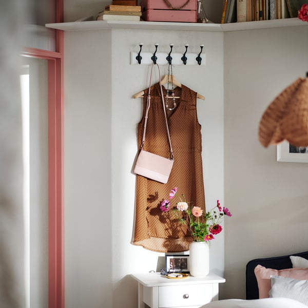 Bruine jurk op een BUMERANG kleerhanger en roze handtas hangen aan een LANDKRABBA rekje met 5 haken aan een witte slaapkamermuur.