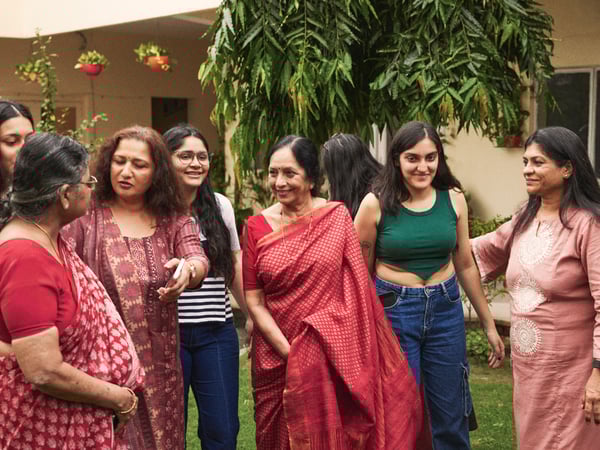 A group of women are standing in a garden in colorful clothes and socializing.