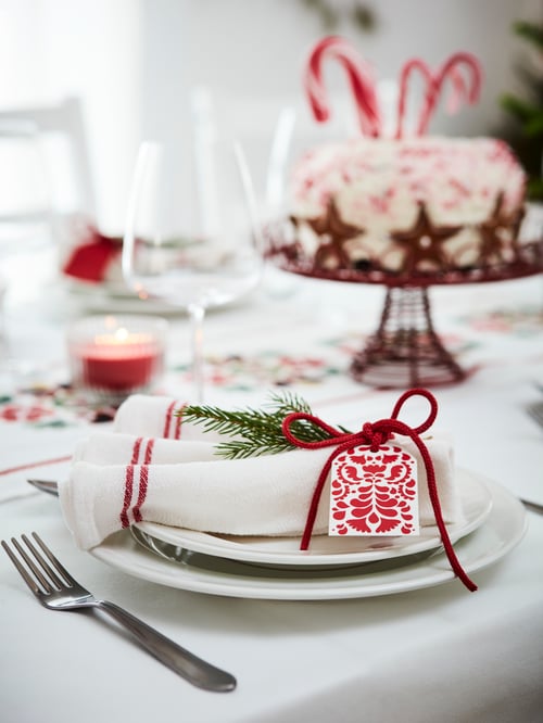 Dining room featuring a flatwoven tea towel in white and red placed on 2 white plates next to a serving stand.