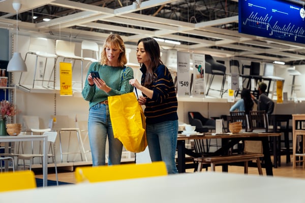 Kaksi henkilöä seisoo IKEA-tavaratalossa ja katsoo puhelinta.