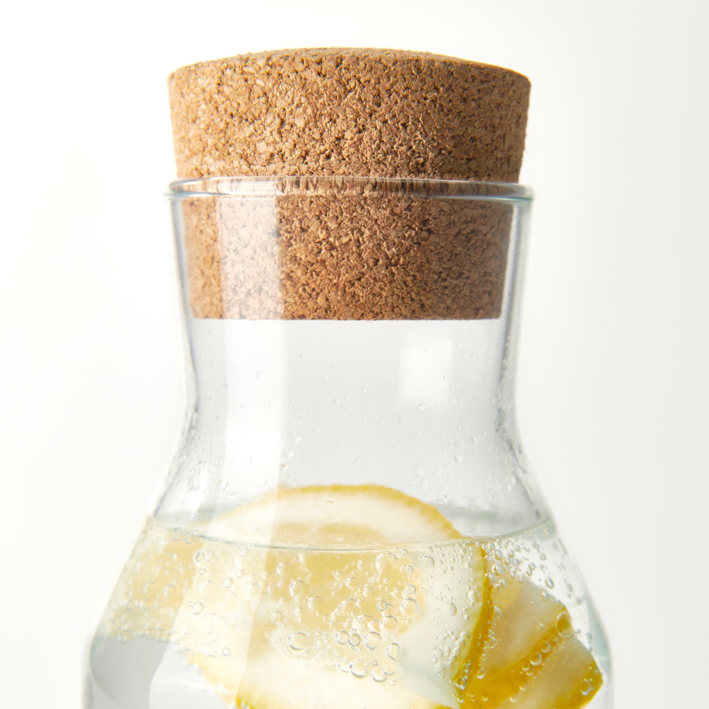 Close-up of the top of an IKEA 365+ glass carafe with cork stopper. It contains sparkling water and slices of lemon.