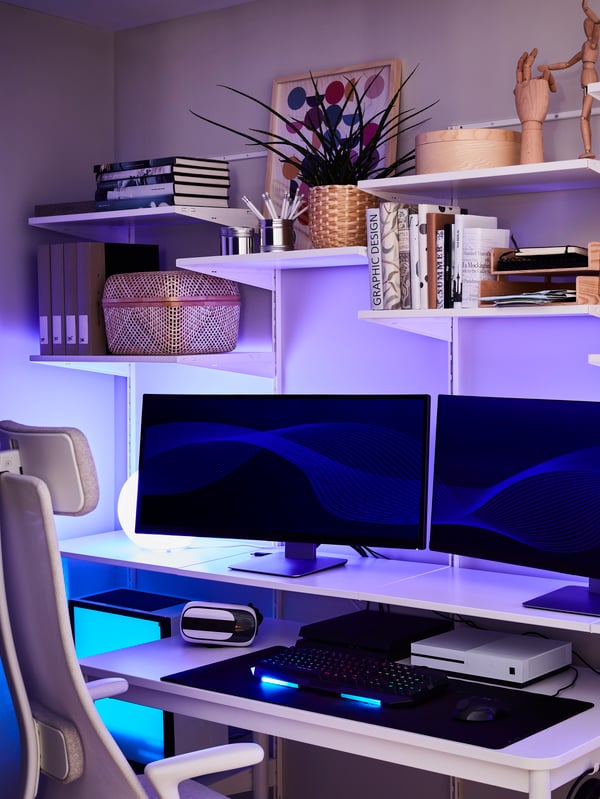 O etajeră cu două monitoare de calculator, cărți, articole decorative și veioze cu lumină albastră. Lângă ea este un scaun de birou.