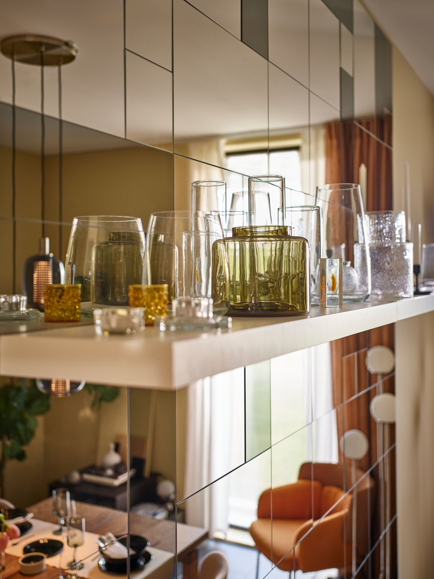 Una cocina moderna con un jarrón KONSTFULL marrón verdoso colocado en una estantería blanca junto a varios jarrones de cristal transparente.