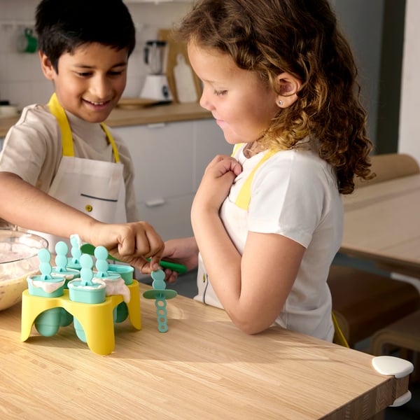 A boy and a girl standing by a kitchen counter making their own ice-cream with the help of UPPFYLLD ice lolly makers.