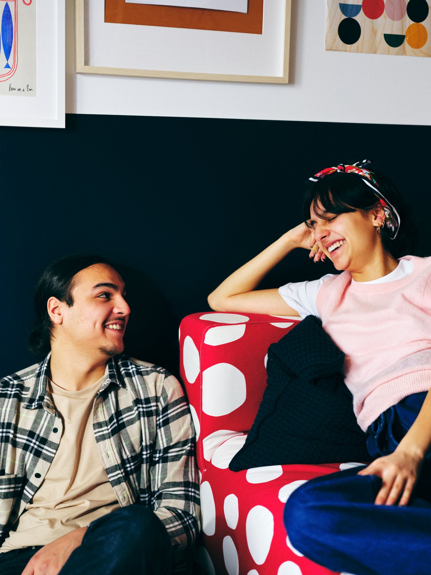 A man and a woman smile at each other, one seated in a red-and-white KLIPPAN two-seat sofa, the other on the floor beside.