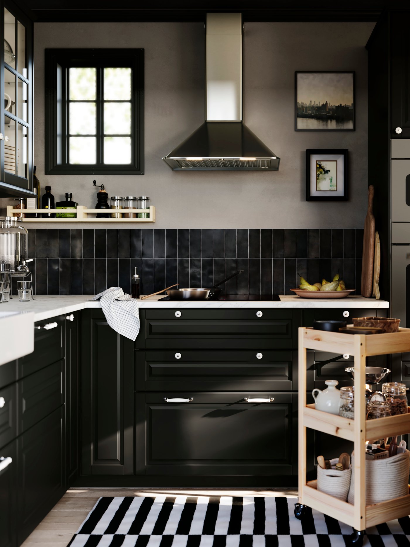 An L-shaped kitchen with black BODBYN drawers has a hob and a MATTRADITION wall mounted extractor hood in stainless steel.