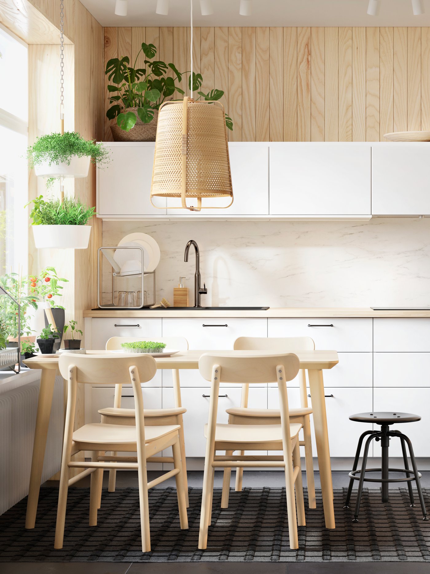 Cocina con mesa, sillas, taburete, lámpara de techo, armarios, grifo, escurreplatos, maceta colgante con plantas naturales.