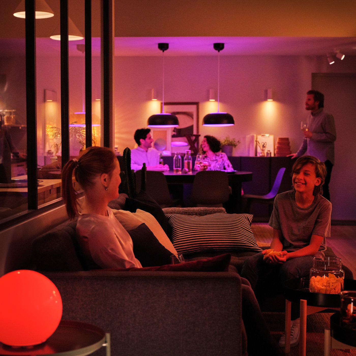 Ett vardagsrum där människor pratar med varandra i stämningsbelysning som skapats av smart belysning från IKEA.