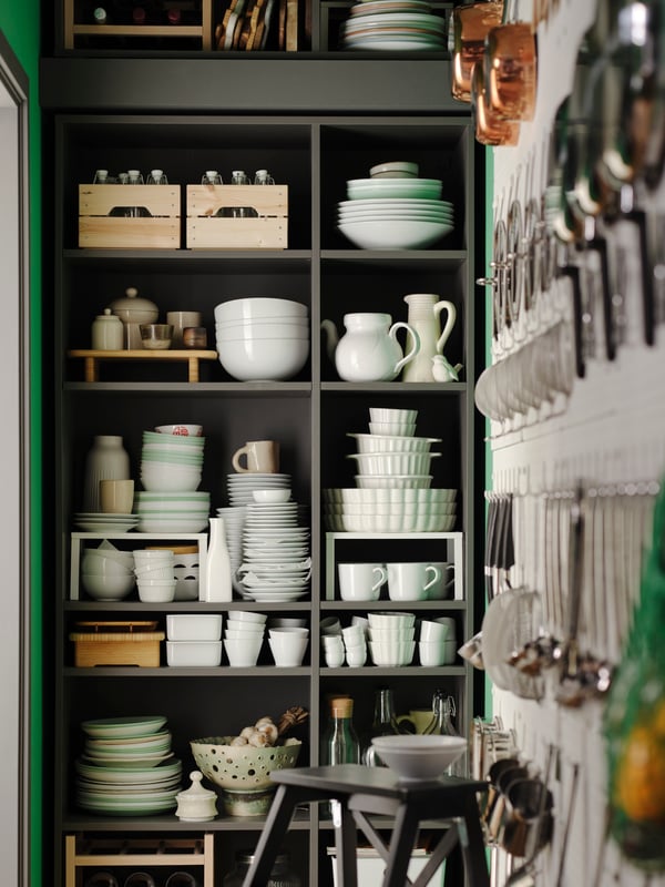 A dark grey VIHALS shelving unit is filled with mainly white dinnerware, but also includes wooden boxes, bottles, and more.