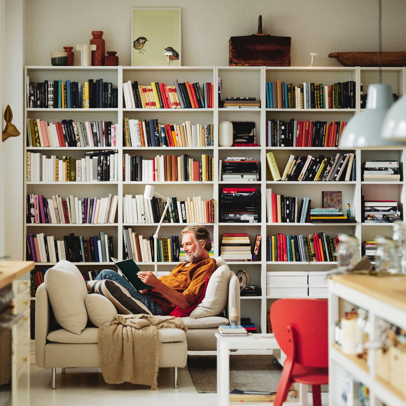 Muž, který si čte knihu u knihovny v obývacím pokoji.