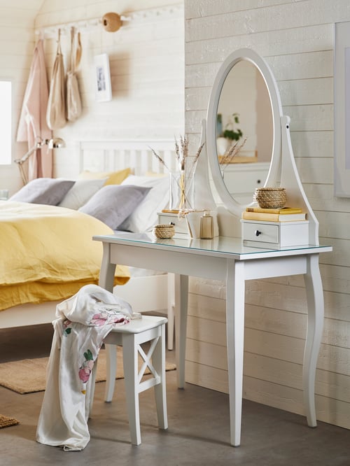Coiffeuse avec miroir intégré HEMNES blanche dans une pièce blanche à côté d’un lit HEMNES avec des oreillers et une couette jaune.