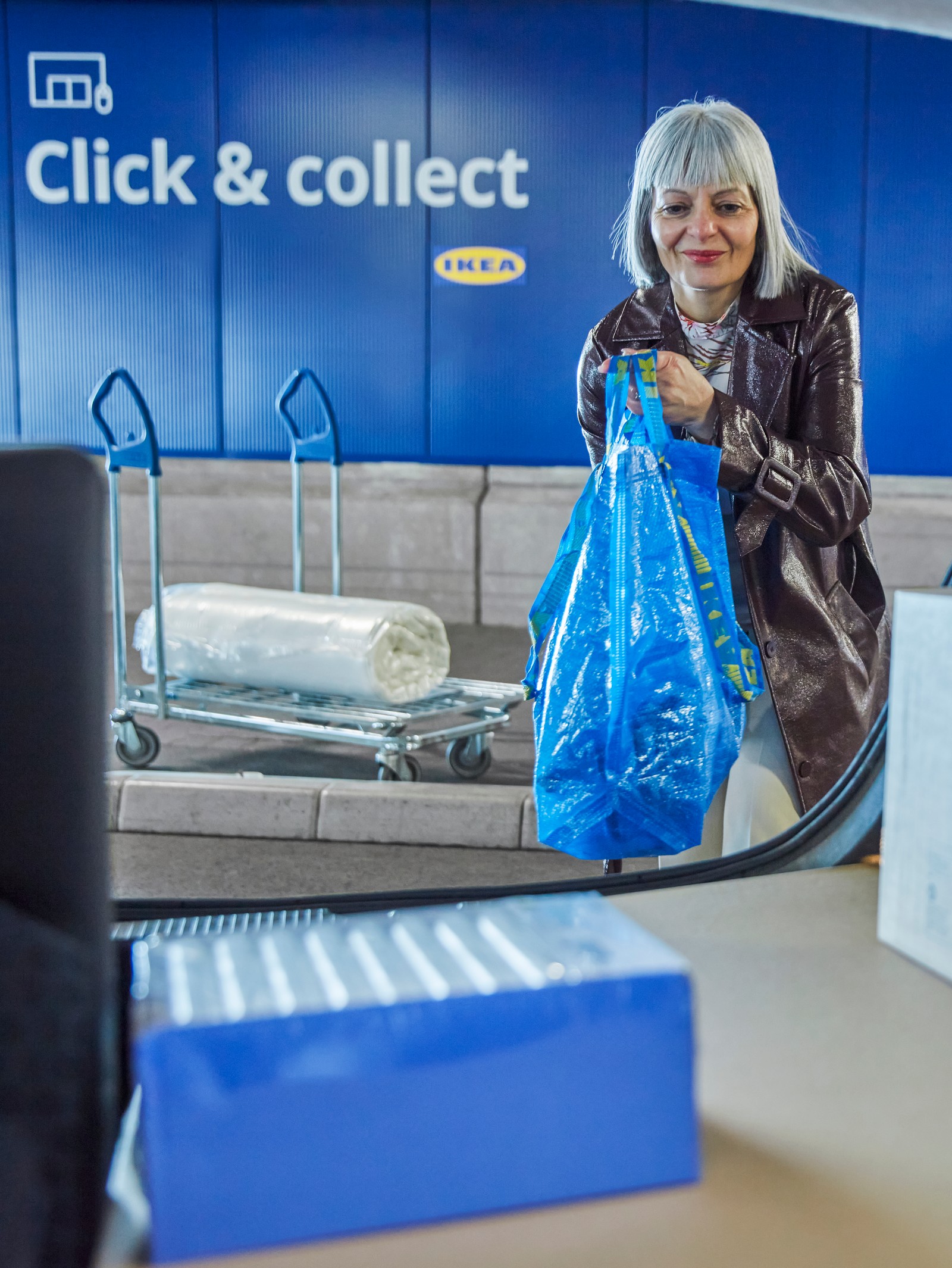 Une personne vue de face en train de charger sa commande Click & Collect dans le coffre d’une voiture.