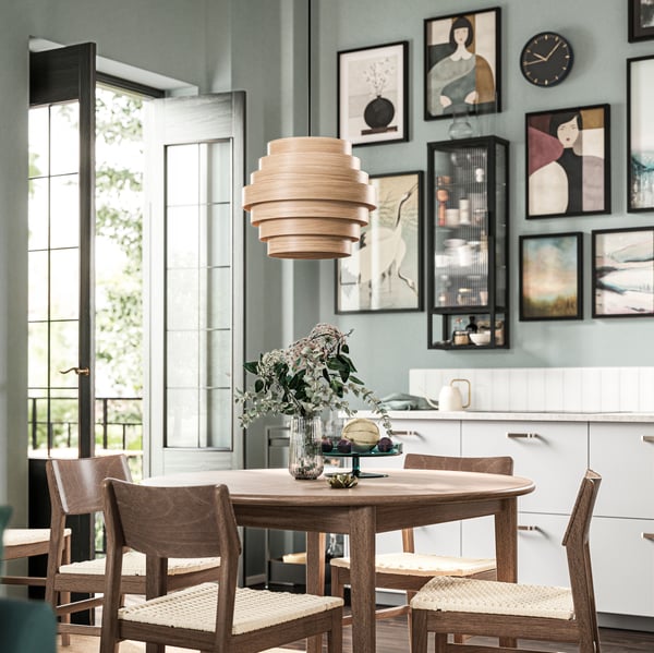 An extendable brown SKANSNÄS table in a dining area, surrounded by four chairs and a backdrop of framed art.