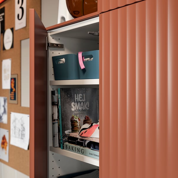 A cabinet door with a TERRSJÖ accent door with a red-brown wave pattern is open, revealing kitchen items stored inside.