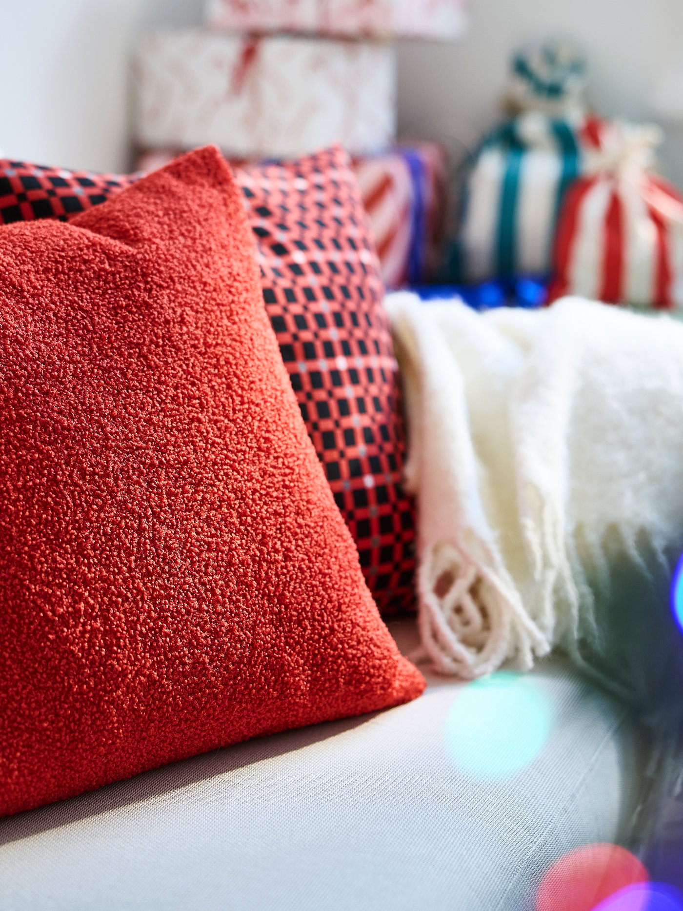 Gemütliche weihnachtliche Textilien mit roten, gemusterten und hellen Kissen auf einem Sofa.