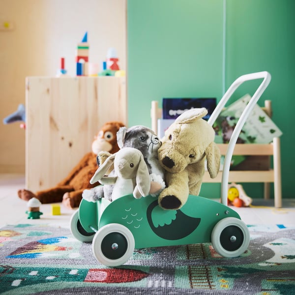 UPPSTÅ toddler walker completely full of soft toys, with a green wall behind it and the VALLABY rug underneath.