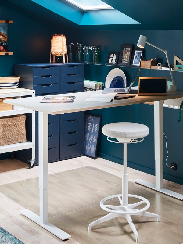 LIDKULLEN sit/stand support by a raised sit/stand desk. Transparent floor protector on the floor.