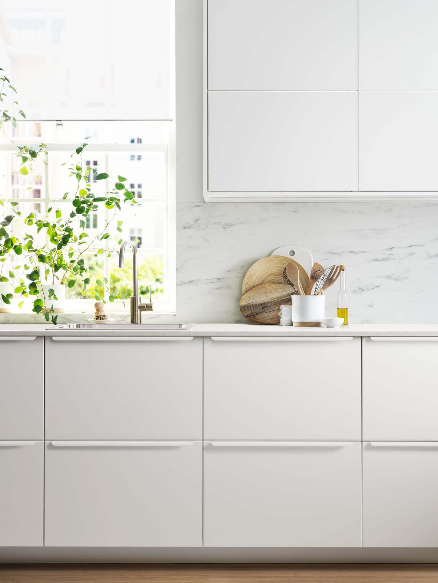 Una cocina elegante con armarios bajos y de pared con frentes blancos, un fregadero y un panel de pared con efecto mármol blanco.