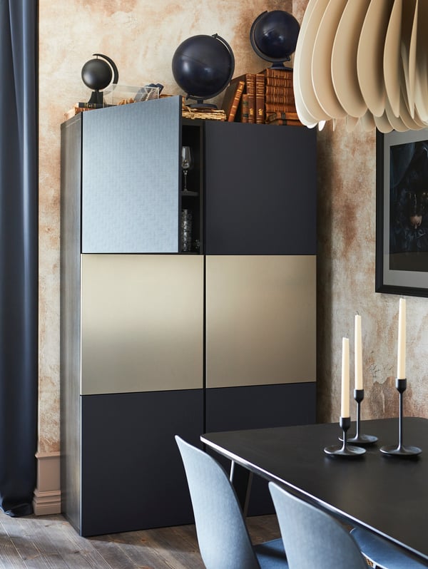 BESTÅ storage combination in black-brown with blue doors, behind a dining table with candle sticks on it and some chairs.