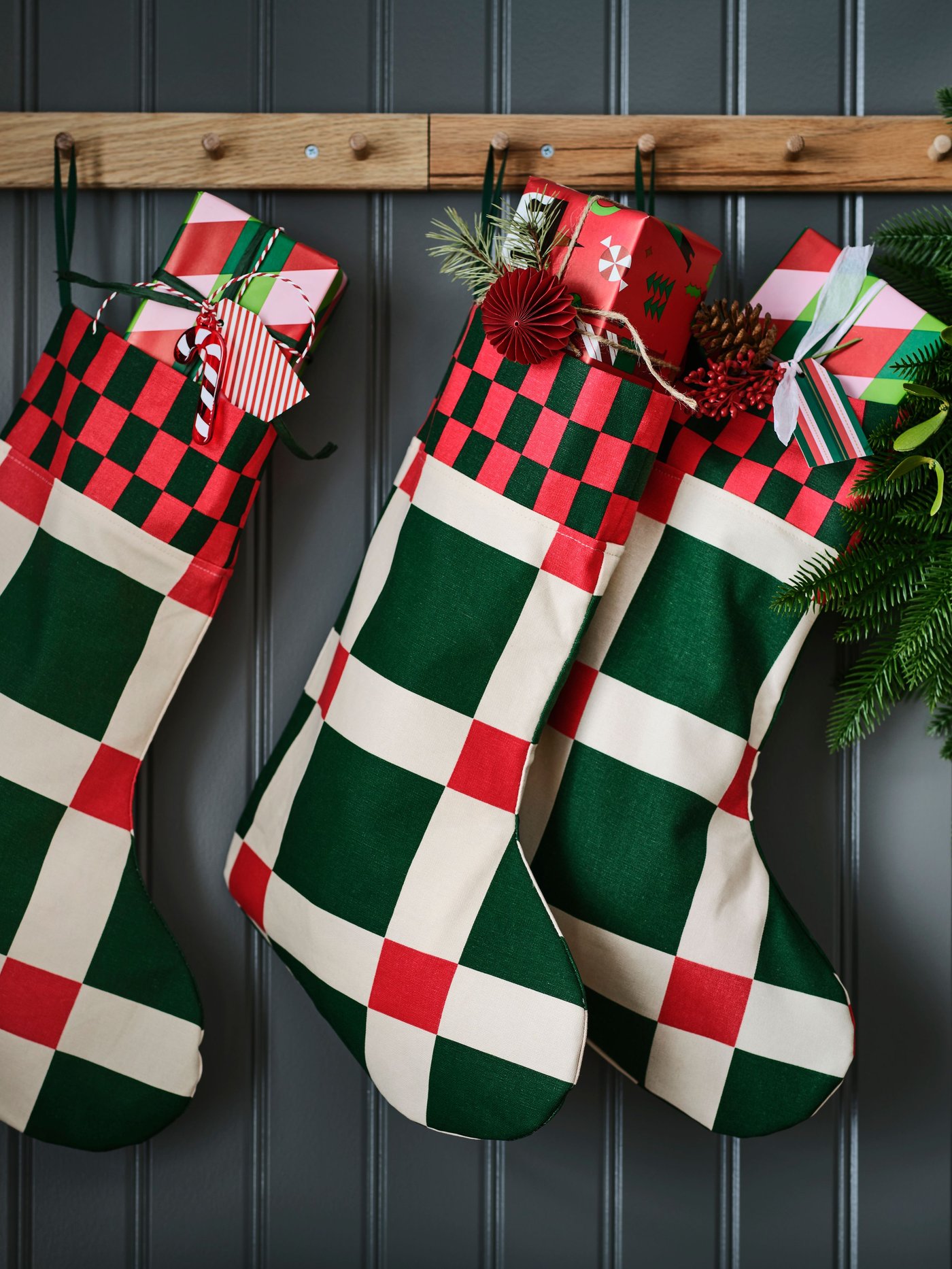 Three VINTERFINT Christmas stockings with a striking green and red check pattern hang on racks with buttons.