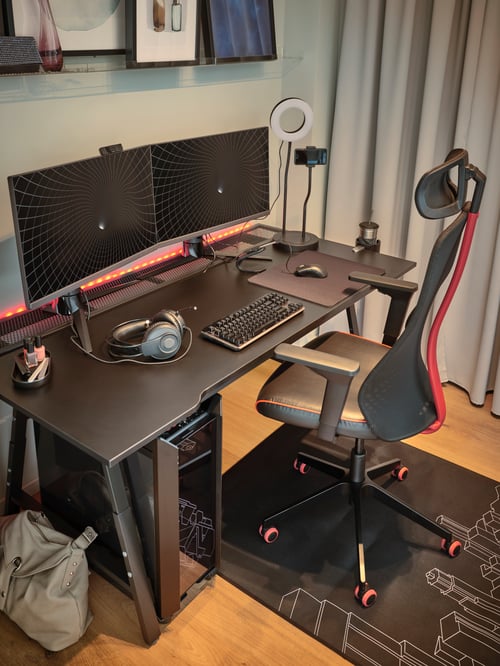 A black MATCHSPEL chair and UTESPELARE desk with a grey curtain on one side and two monitors and a ring light on top.
