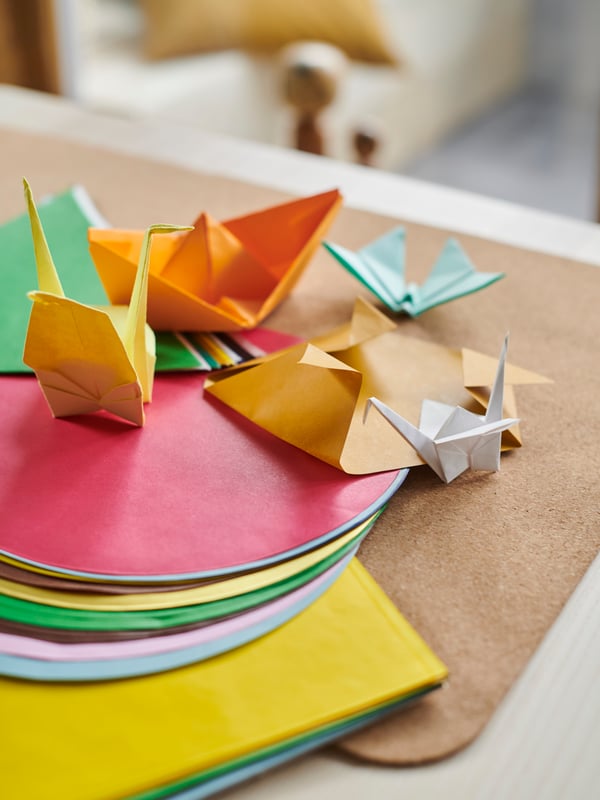 A table top holding multicoloured LUSTIGT origami paper in different shapes, as well as some completed origami objects.