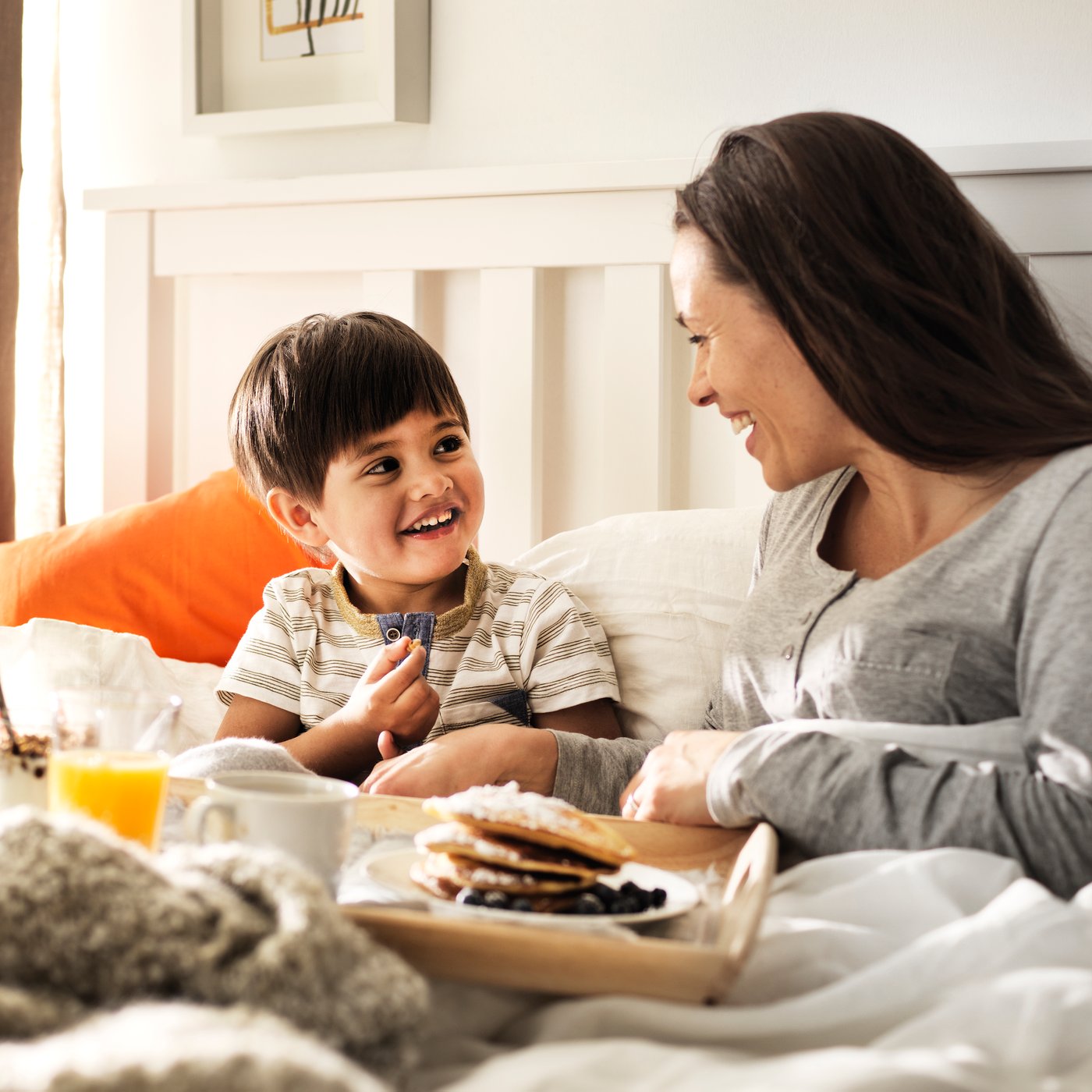 Une mère et son enfant assis dans un lit, avec un plateau de déjeuner posé devant eux.