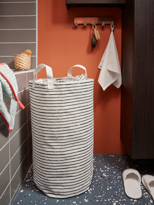 Baie cu sac de rufe cu model învelit, prosoape de mână pe umeraș cu mânere, o pereche de papuci, un ghiveci, perii.