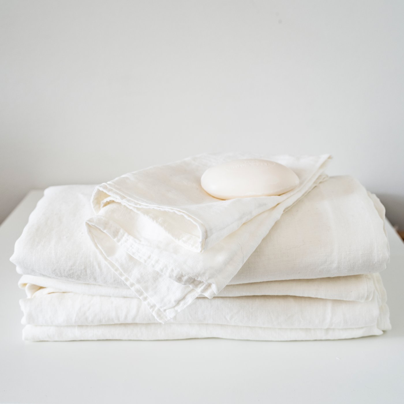 Gefaltete weiße Stofflagen mit einem Stück Seife darauf auf hellem Hintergrund