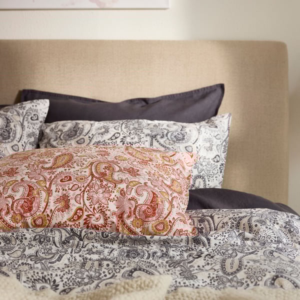 The top of a bed that’s covered with two types of RODGERSIA paisley pattern bed linen, one in grey and the other in red.