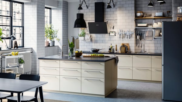 A modern IKEA HAVSTORP matt beige kitchen with an island, dark worktop, black appliances and steel handles.