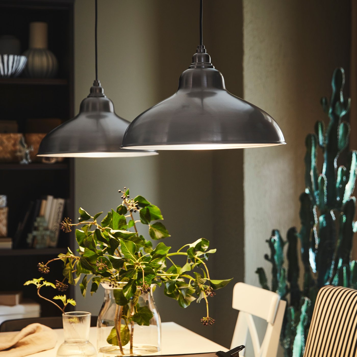 Två ANKARSPEL pendellampor hänger ovanför ett vitt utdragbart INGATORP bord med böcker och vaser ovanpå.