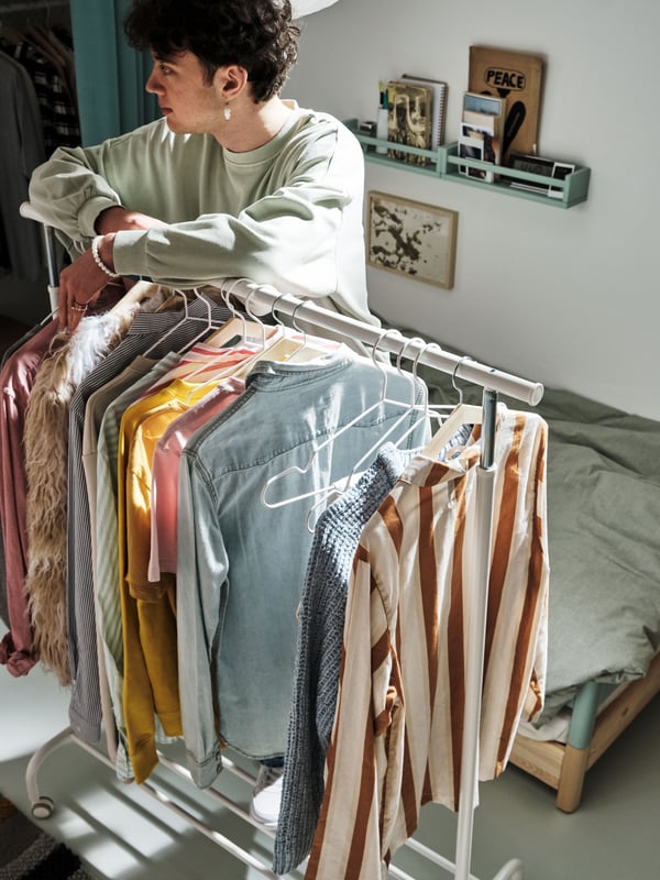 Boy leaning on a rail with clothes hanging on it.