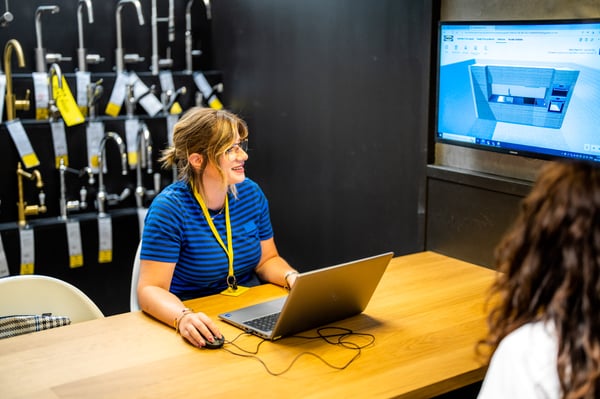 Ein IKEA-Mitarbeiter an einem Tisch mit einem Laptop, im Hintergrund sitzt eine Frau.